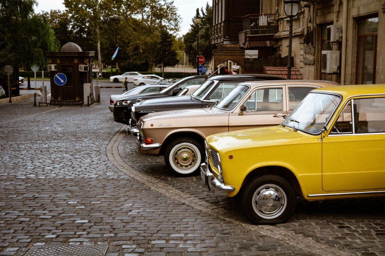 A row of colorful classic vintage cars parked on a cobbled street in a historic area.